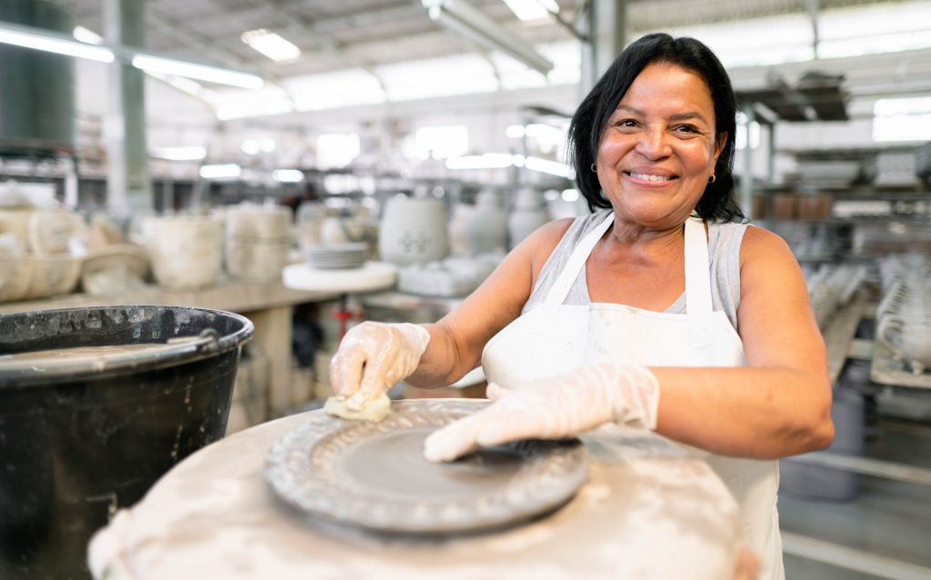 Portrait of a smiling female worker cleaning a clay plate while working in a ceramics manufacturing workshop